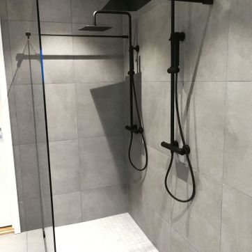 Moderne dusj med glass, grå fliser på vegg og sorte detaljer